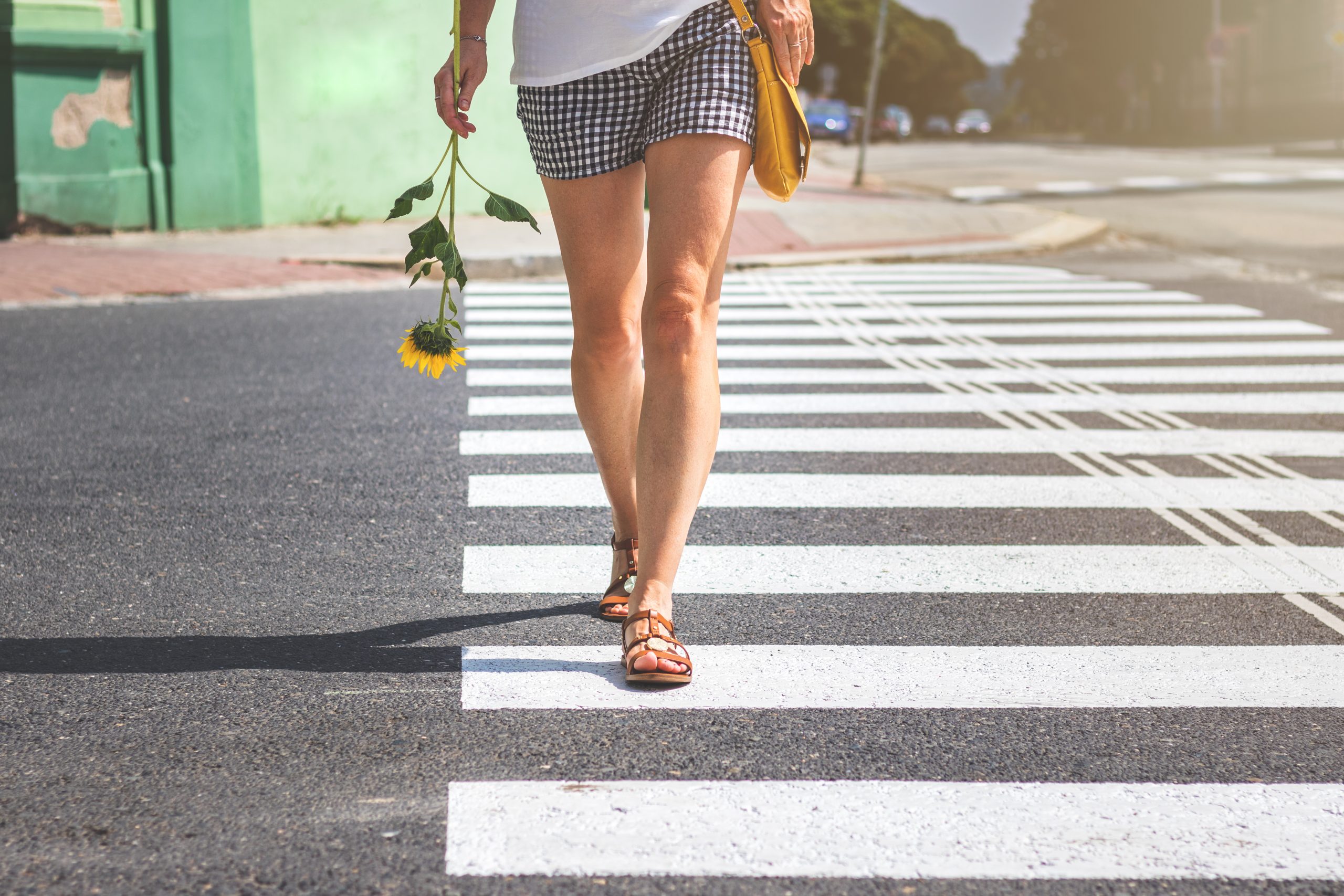 spider veins; Legs of young woman wearing shorts and sandals is crossing street on zebra marking.